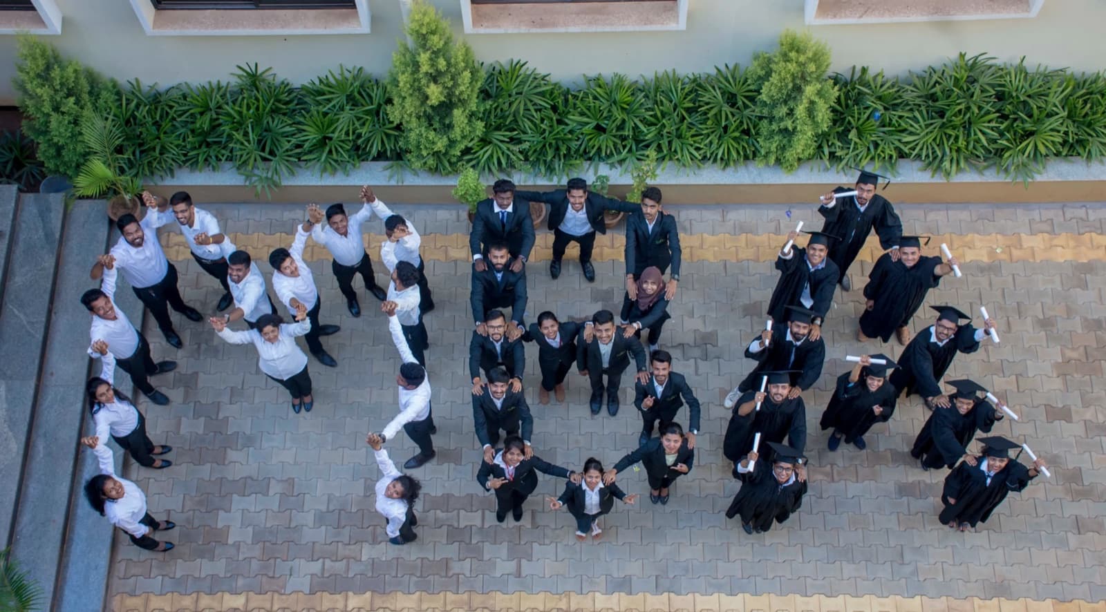 IBMR students in business suits and graduation gowns, photographed from above in the campus courtyard